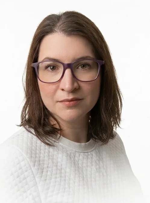 Retrato de Natalia Caballero: cabelos castanhos na altura dos ombros, óculos de armação roxa e blusa branca.